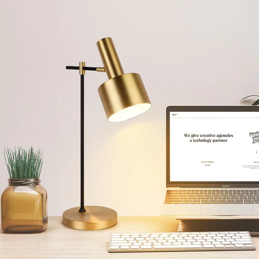Modern light luxury black-gold adjustable metal table lamp, golden lampshade + black-gold stand + round golden base, angle-adjustable, soft warm light, creating a simple high-end office/home atmosphere.