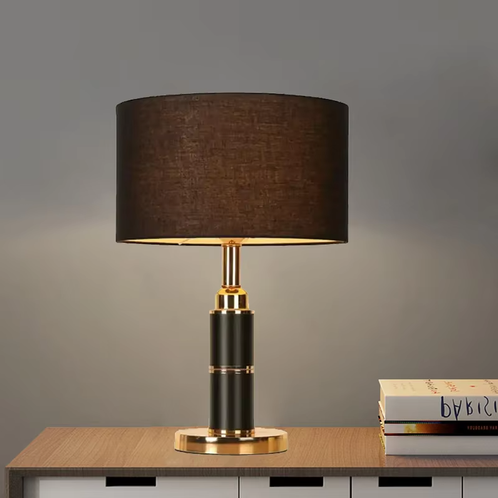 Light luxury black-gold cylindrical base table lamp, black main column + golden metal decorations + beige fabric lampshade, soft warm light creates a high-end home atmosphere.