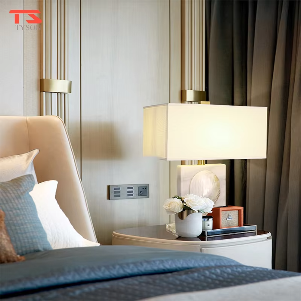 This light luxury modern table lamp features a light-colored stone base with shell relief, paired with gold metal connectors and an off-white fabric rectangular lampshade. It serves both lighting and decorative purposes, ideal for light luxury spaces such as bedroom bedside tables, living room side tables, and hotel guest rooms.