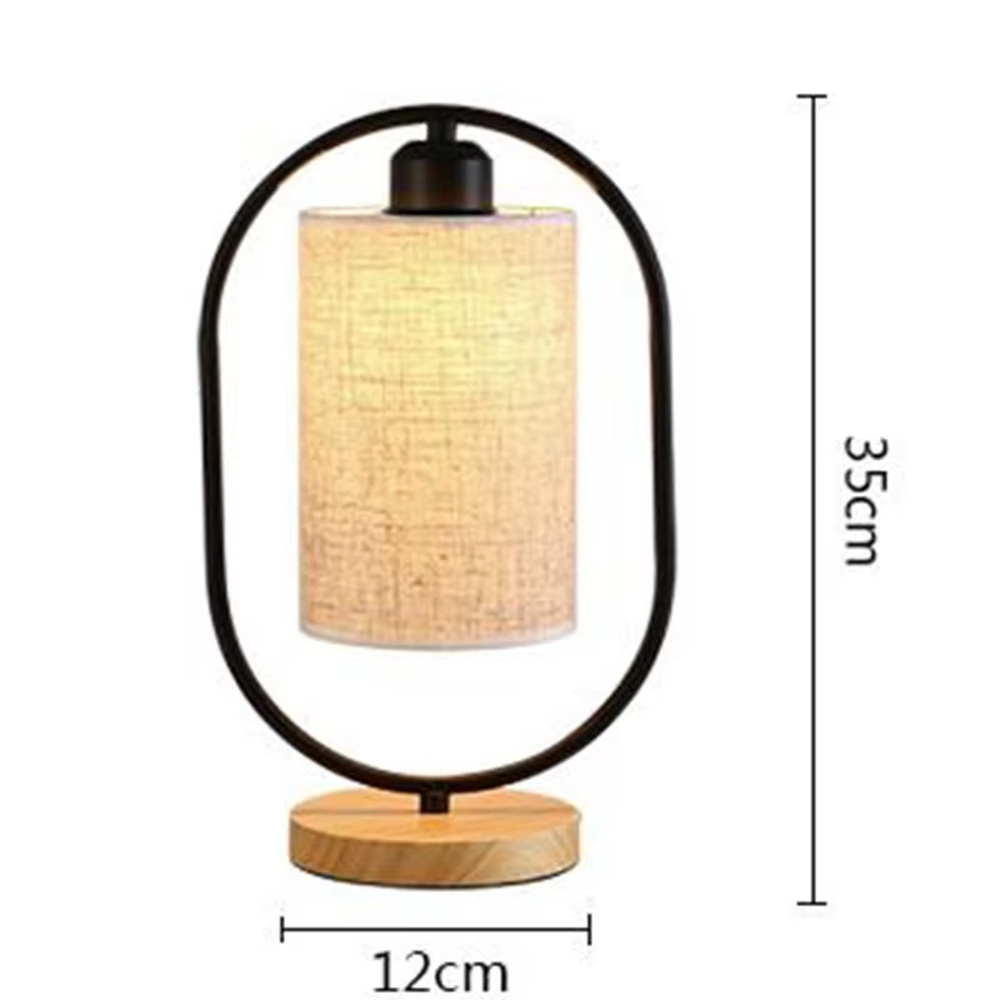 This is a modern minimalist oval frame table lamp, with a black metal oval stand paired with a beige linen lampshade and a solid wood base, featuring both decorative and lighting functions, ideal for warm indoor scenarios such as bedroom nightstands and living room side tables.