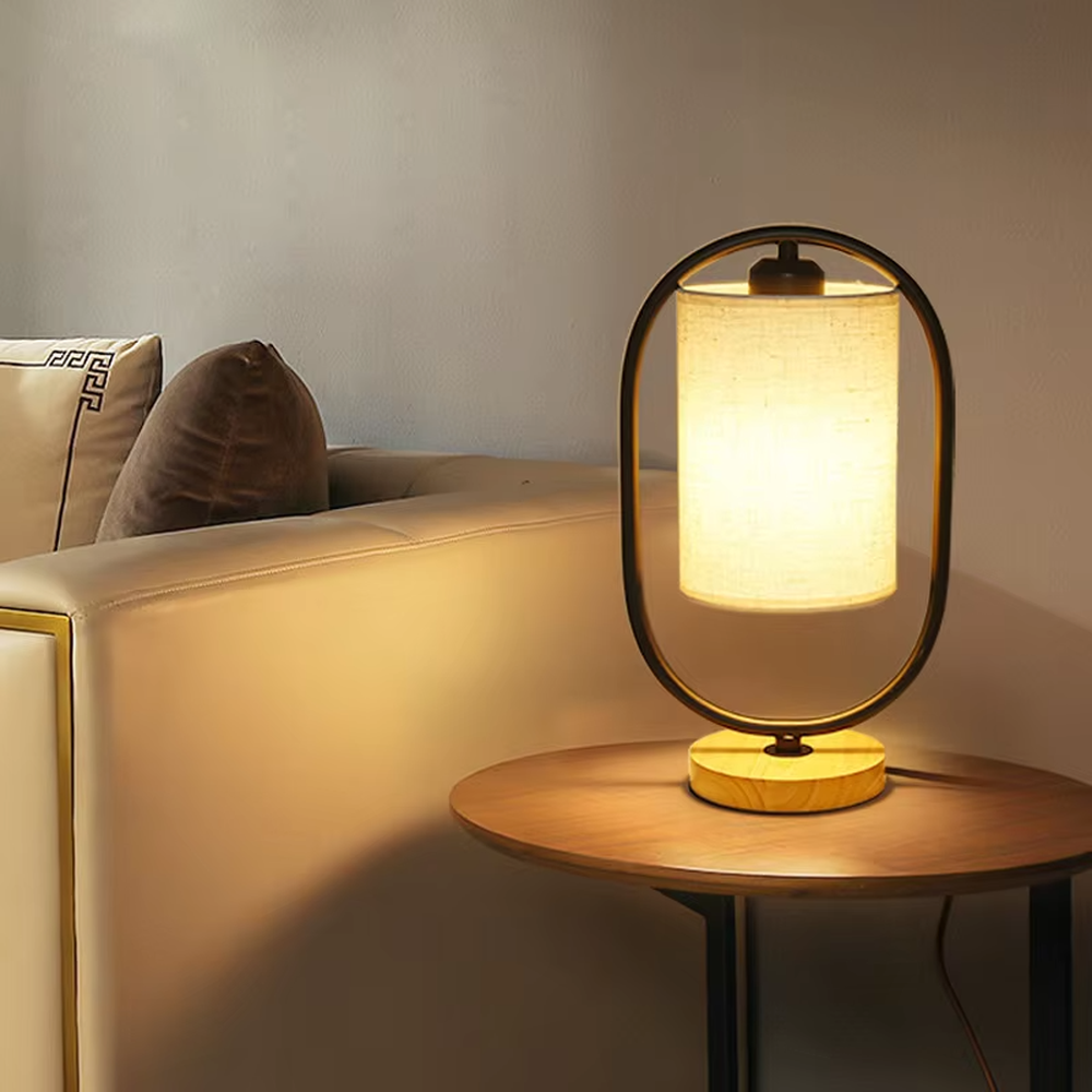 Modern minimalist silver oval metal frame linen texture lampshade wooden base table lamp, warm light effect, creating a cozy minimalist home atmosphere.