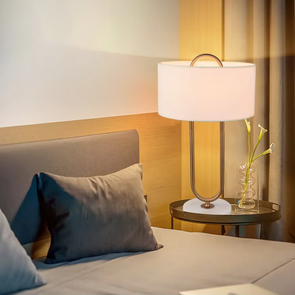 This modern light luxury table lamp features a U-shaped frame made of gold metal, paired with a white fabric rectangular lampshade and a white marble base, with a simple and elegant shape. It serves both lighting and decorative purposes, ideal for light luxury spaces such as bedroom bedside tables, living room side tables, and hotel guest rooms.