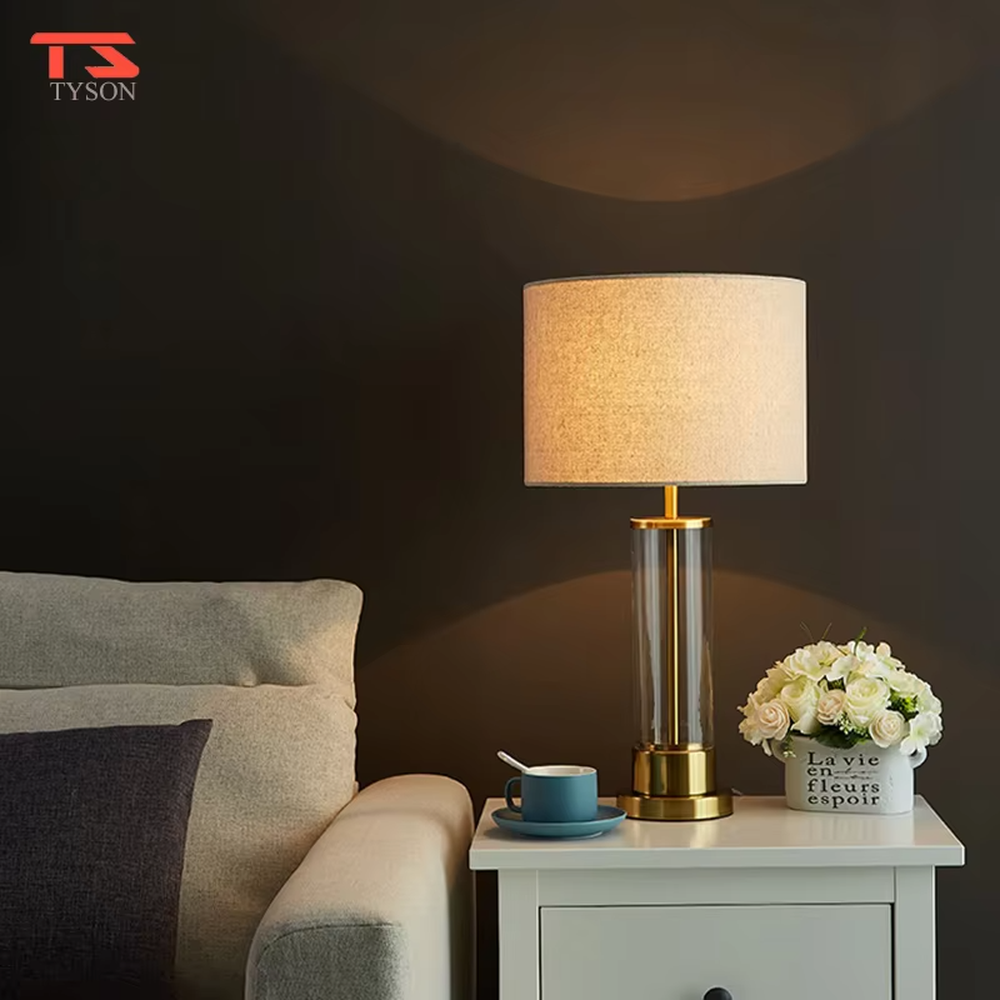 This modern light luxury table lamp features a transparent glass lamp body, paired with gold metal connectors and base, and an off-white fabric cylindrical lampshade that transmits light softly. It serves both lighting and decorative purposes, ideal for light luxury spaces such as bedroom bedside tables, living room side tables, and hotel guest rooms.