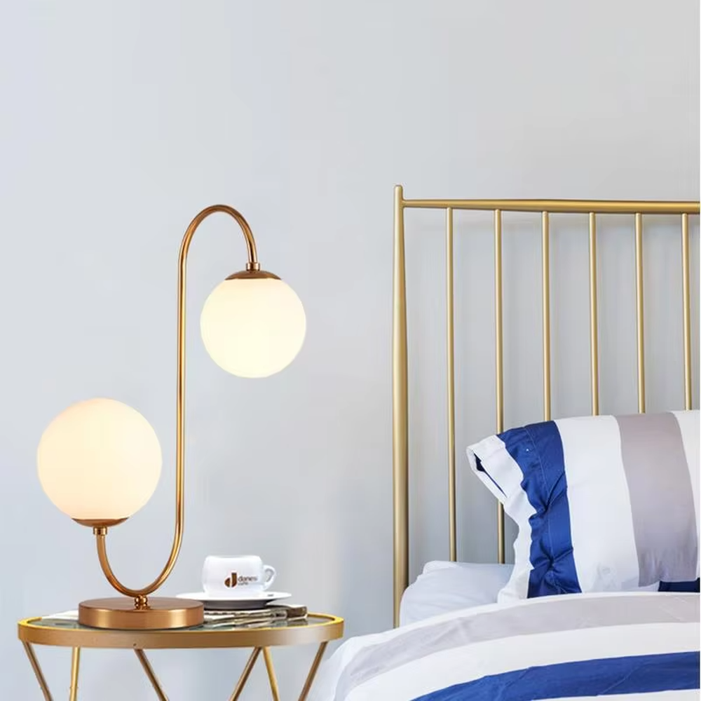 Light luxury double-ball curved table lamp (gold metal curved bracket + double milk-white glass ball lampshades + round metal base), warm light effect, creating a modern and elegant home atmosphere.