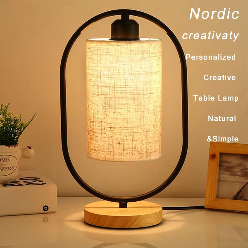 This is a modern minimalist oval frame table lamp, with a black metal oval stand paired with a beige linen lampshade and a solid wood base, featuring both decorative and lighting functions, ideal for warm indoor scenarios such as bedroom nightstands and living room side tables.