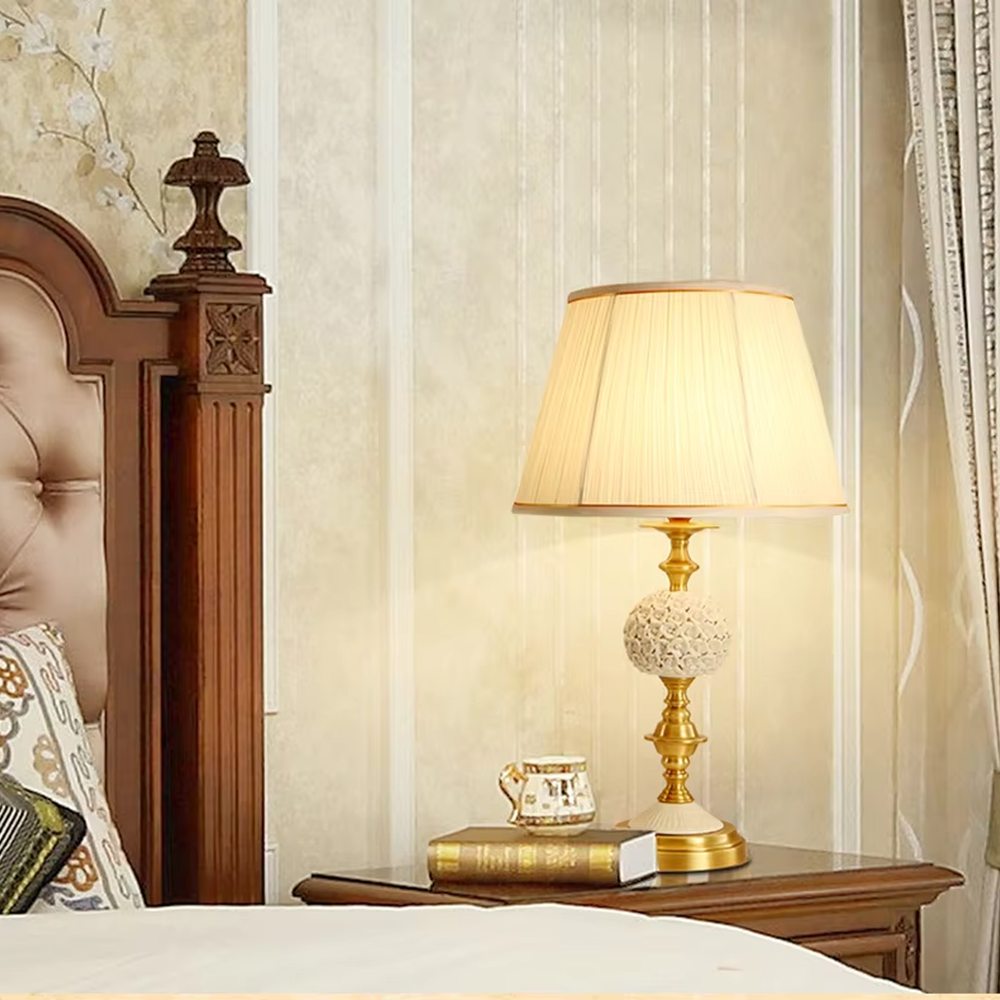 This European light luxury table lamp features a glossy gold metal base, paired with hollow carved crystal decorations and an off-white pleated fabric lampshade, presenting a luxurious and retro court texture. The light is soft and warm, serving both lighting and decorative purposes, suitable for placement in European-style spaces such as bedrooms and villa guest rooms.