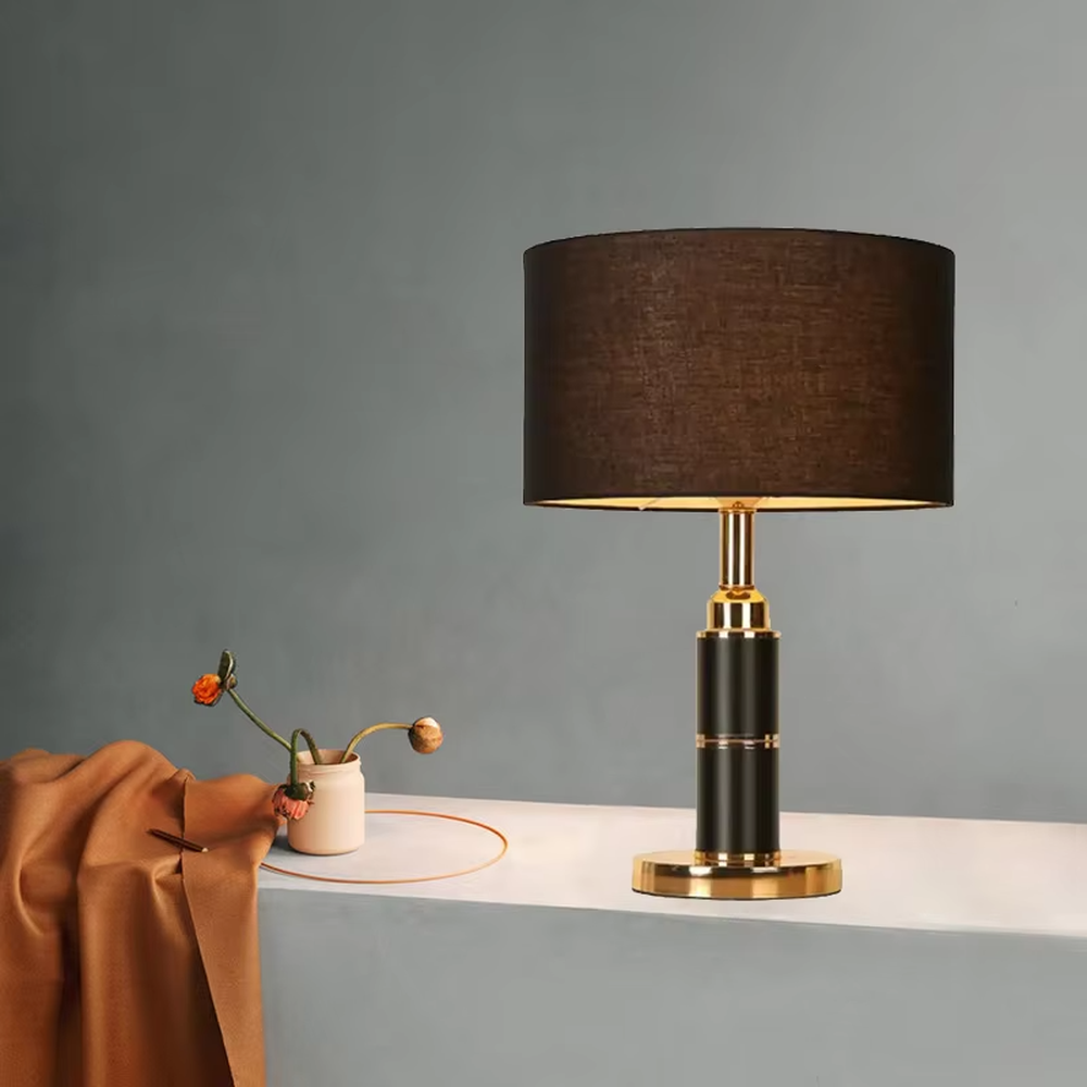 Light luxury black-gold cylindrical base table lamp, black main column + golden metal decorations + beige fabric lampshade, soft warm light creates a high-end home atmosphere.