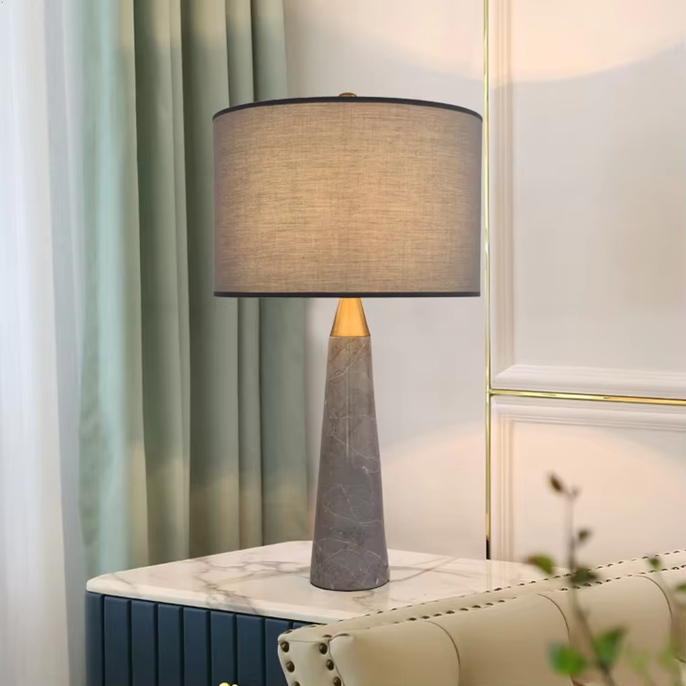 Light luxury marble cone table lamp, with a grey natural marble base, gold metal connection, off-white fabric lampshade with black trim, providing soft and warm light, designed to enhance the delicate texture of spaces, suitable for bedroom nightstands, living room side tables, modern light luxury homes and hotel guest rooms, etc.