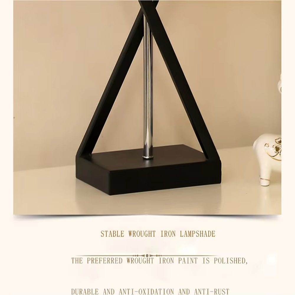 This is a modern minimalist fabric table lamp, featuring an off-white linen lampshade paired with a geometric cross-shaped white and silver dual-color lamp base, which has both lighting and decorative functions, suitable for bedroom nightstands, study desks, hotel guest rooms and other spaces.