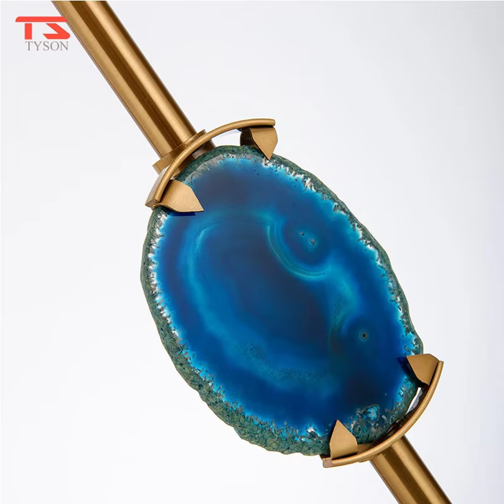 This is a light luxury agate decorative table lamp, with an off-white fabric lampshade paired with a gold metal lamp pole, inlaid with a natural blue agate slice in the middle, and a transparent crystal square base, featuring both decorative and lighting functions, ideal for high-end indoor scenarios such as bedroom nightstands and living room side tables.