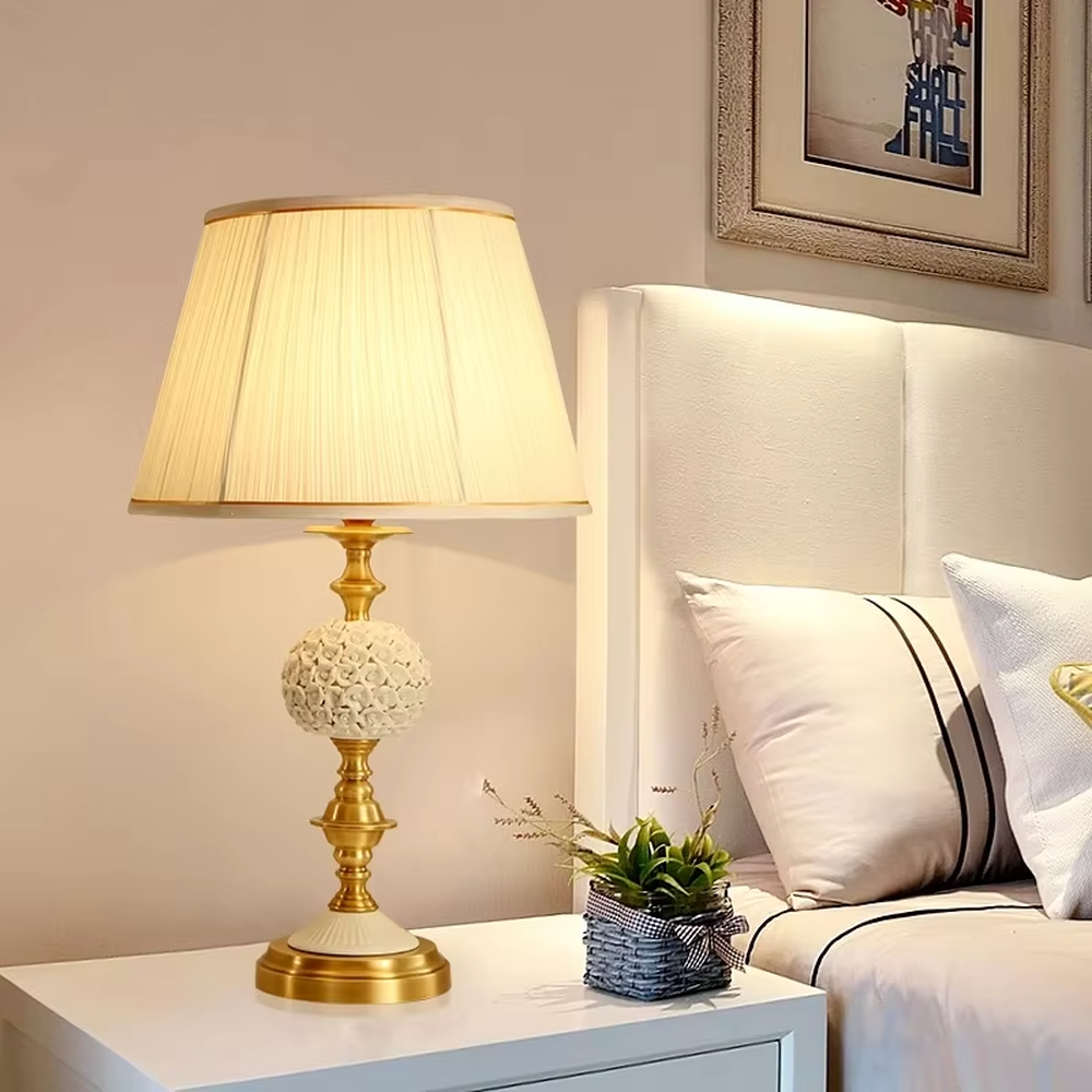 This European light luxury table lamp features a glossy gold metal base, paired with hollow carved crystal decorations and an off-white pleated fabric lampshade, presenting a luxurious and retro court texture. The light is soft and warm, serving both lighting and decorative purposes, suitable for placement in European-style spaces such as bedrooms and villa guest rooms.