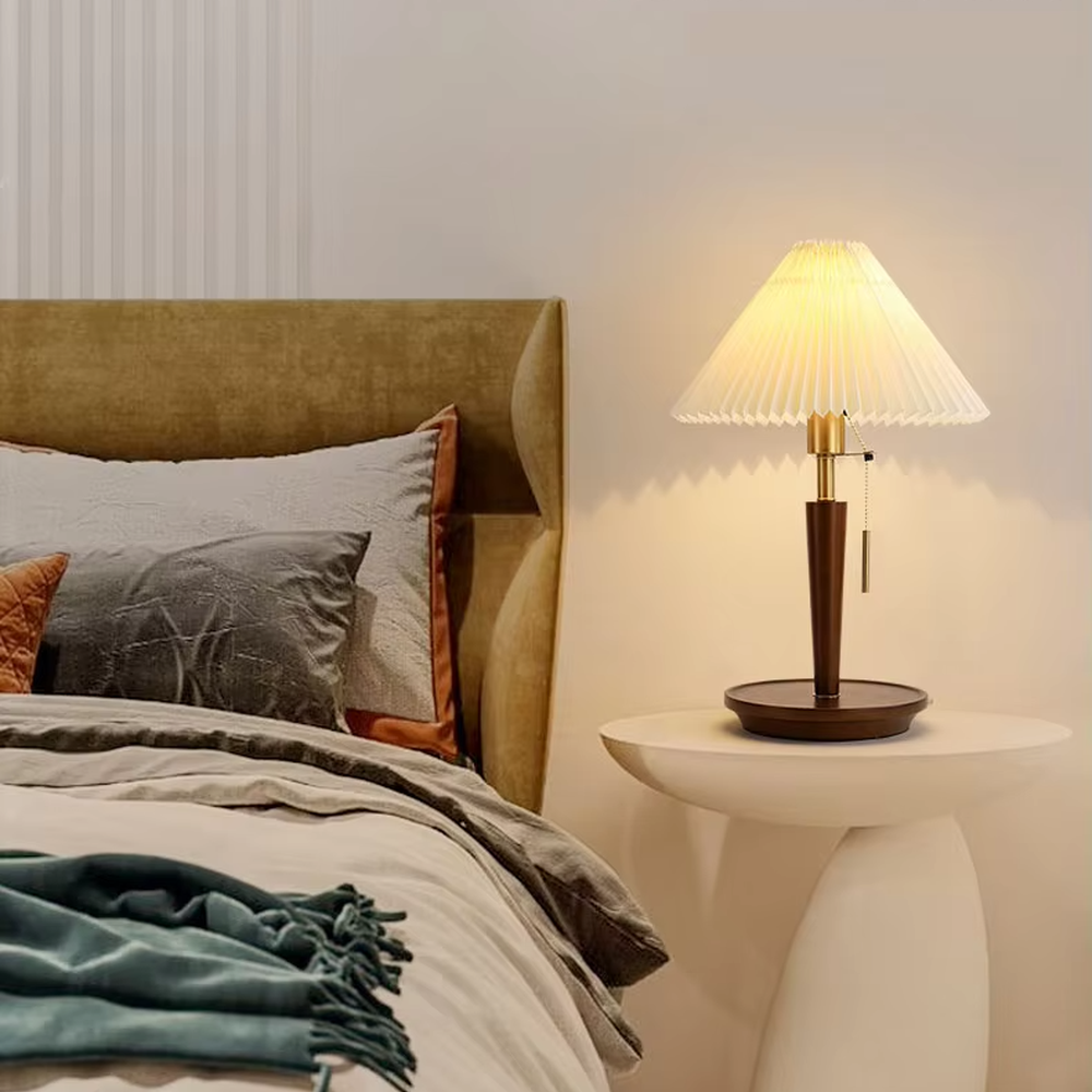 Vintage Nordic pleated fabric table lamp, with an off-white pleated fabric lampshade paired with a dark brown wood and gold metal spliced lamp pole, featuring a pull-cord switch, emitting soft and warm light, combining decorativeness and practicality, suitable for lighting and decoration in spaces such as bedroom nightstands, living room side tables, and B&B guest rooms.