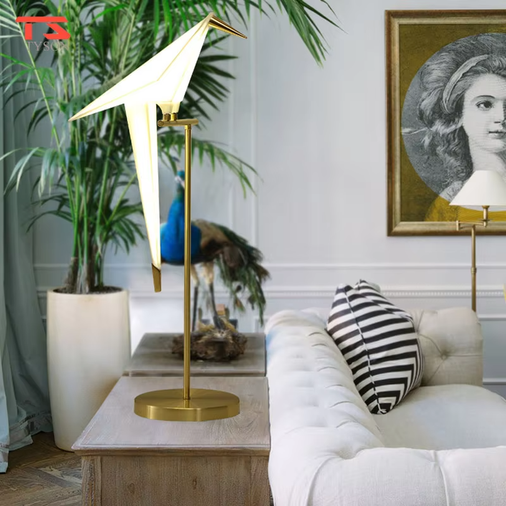 This is a modern light luxury origami crane-shaped table lamp, featuring a gold metal stand paired with a translucent paper art lamp body. The lamp body is as dynamic and soft as an origami crane, serving both lighting and artistic decoration purposes, suitable for bedroom nightstands, light luxury living room side tables, hotel guest rooms, showrooms and other scenarios.