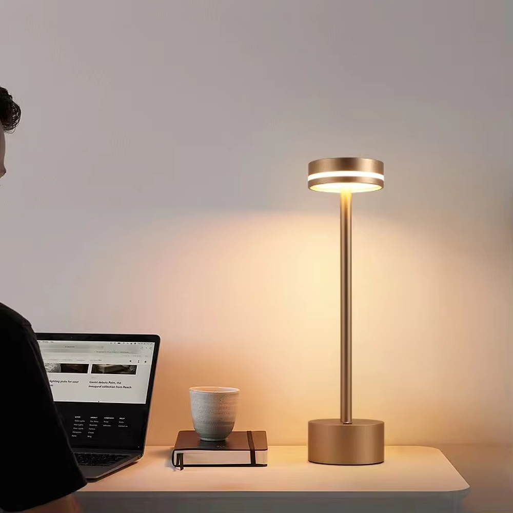 Modern minimalist bronze metal rechargeable table lamp, featuring a cylindrical lamp body and a top ring-shaped lighting design, emitting soft and even light. It supports wireless battery life and touch dimming, suitable for ambient lighting and supplementary lighting in scenarios such as dining tables, bars, and bedroom nightstands.