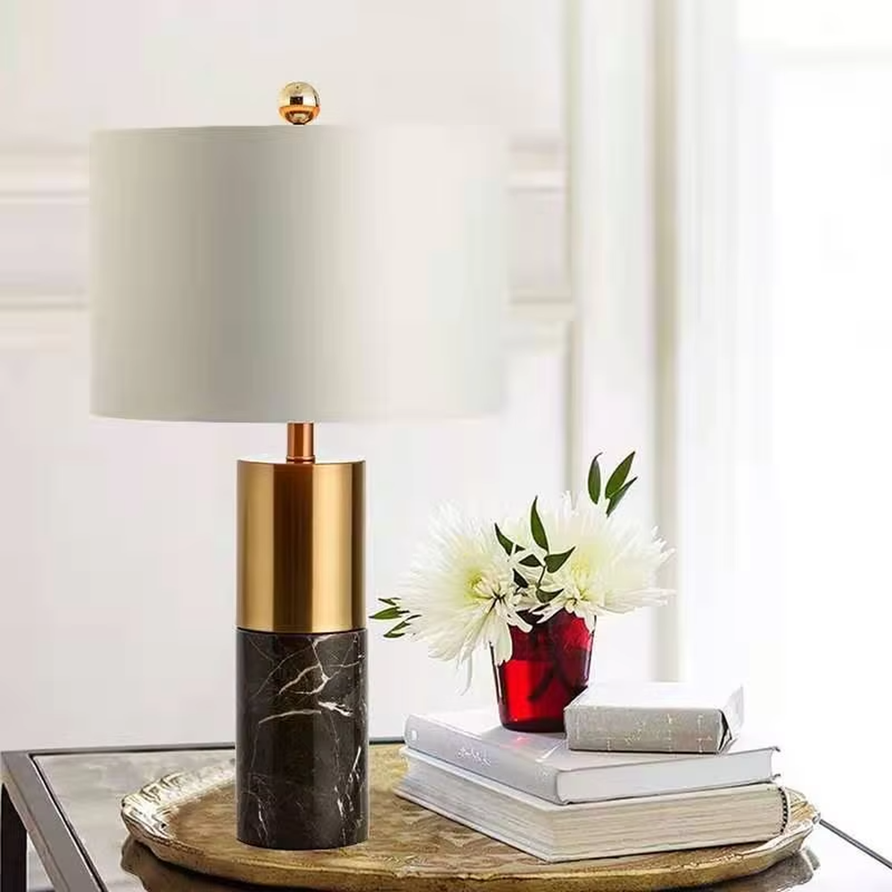 This light luxury table lamp features a black marble (with white veins) base, paired with a gold metal cylindrical lamp body and an off-white fabric cylindrical lampshade, with a gold spherical decoration on top. It serves both lighting and decorative purposes, ideal for light luxury spaces such as bedroom bedside tables, living room side tables, and hotel guest rooms.