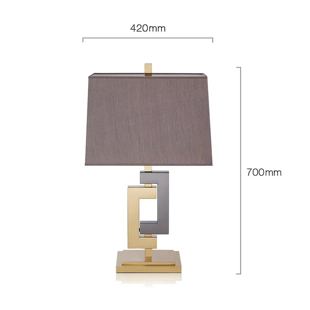 This is a modern light luxury geometric interlocking table lamp, featuring an interlocking geometric lamp body crafted from gold and gray dual-color metal, paired with a dark gray fabric lampshade. It emits soft and uniform light, serving both lighting and decorative purposes, suitable for bedroom nightstands, light luxury living room side tables, hotel guest rooms, showrooms and other scenarios.