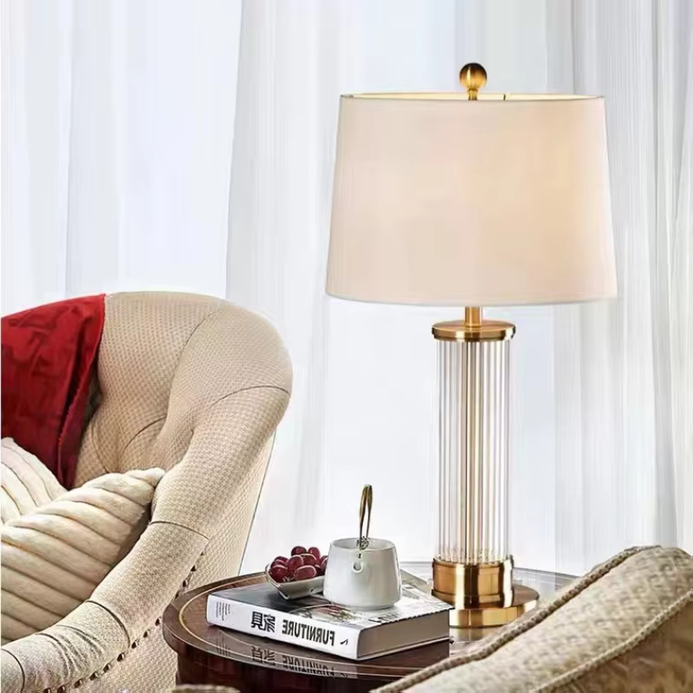 This is a light luxury crystal metal table lamp, with an off-white fabric lampshade edged with gold trim, a lamp post made of vertical striped transparent crystal paired with gold metal splicing, and a gold metal base, featuring both decorative and lighting functions, ideal for high-end indoor scenarios such as bedroom nightstands and living room side tables.