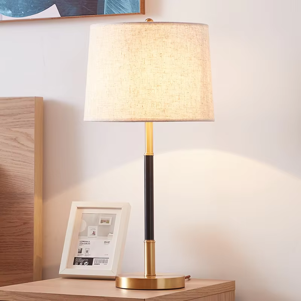This is a minimalist light luxury table lamp, featuring an off-white linen fabric lampshade paired with a black and gold dual-color metal lamp pole, with a pull-chain switch. It emits soft and warm light, serving both lighting and decorative purposes, suitable for bedroom nightstands, living room side tables, studies, hotel guest rooms and other scenarios.