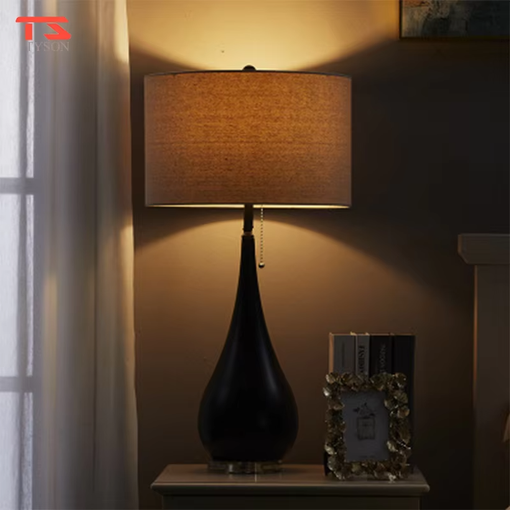 This is a pastoral-style floral fabric table lamp, with an off-white lampshade printed with blue and black floral patterns, paired with a black matte teardrop-shaped base and transparent crystal feet, featuring both decorative and lighting functions, ideal for warm indoor scenarios such as bedroom nightstands and living room side tables.