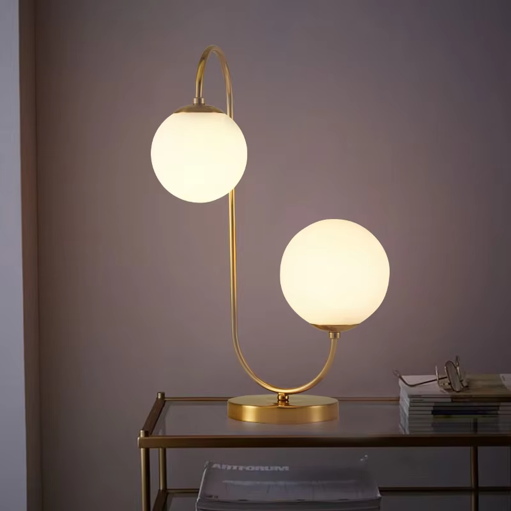 Light luxury double-ball curved table lamp (gold metal curved bracket + double milk-white glass ball lampshades + round metal base), warm light effect, creating a modern and elegant home atmosphere.