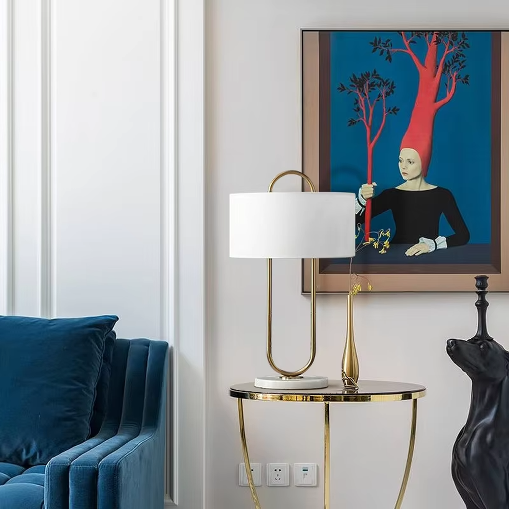 This modern light luxury table lamp features a U-shaped frame made of gold metal, paired with a white fabric rectangular lampshade and a white marble base, with a simple and elegant shape. It serves both lighting and decorative purposes, ideal for light luxury spaces such as bedroom bedside tables, living room side tables, and hotel guest rooms.