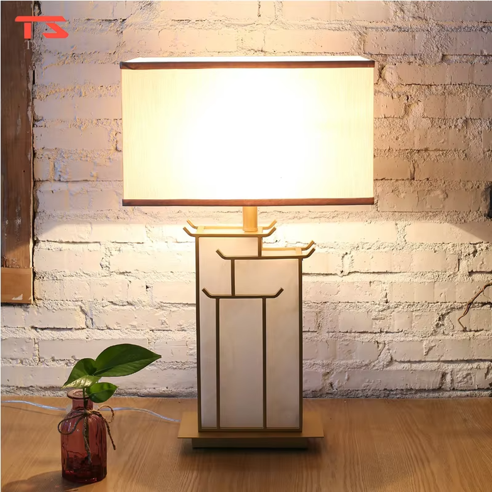 This is a new Chinese style table lamp, featuring a rectangular fabric lampshade paired with a geometric splicing base with Chinese architectural elements, which has both lighting and decorative functions, suitable for bedrooms, studies, tea rooms, new Chinese-style homes and hotel guest rooms and other spaces.