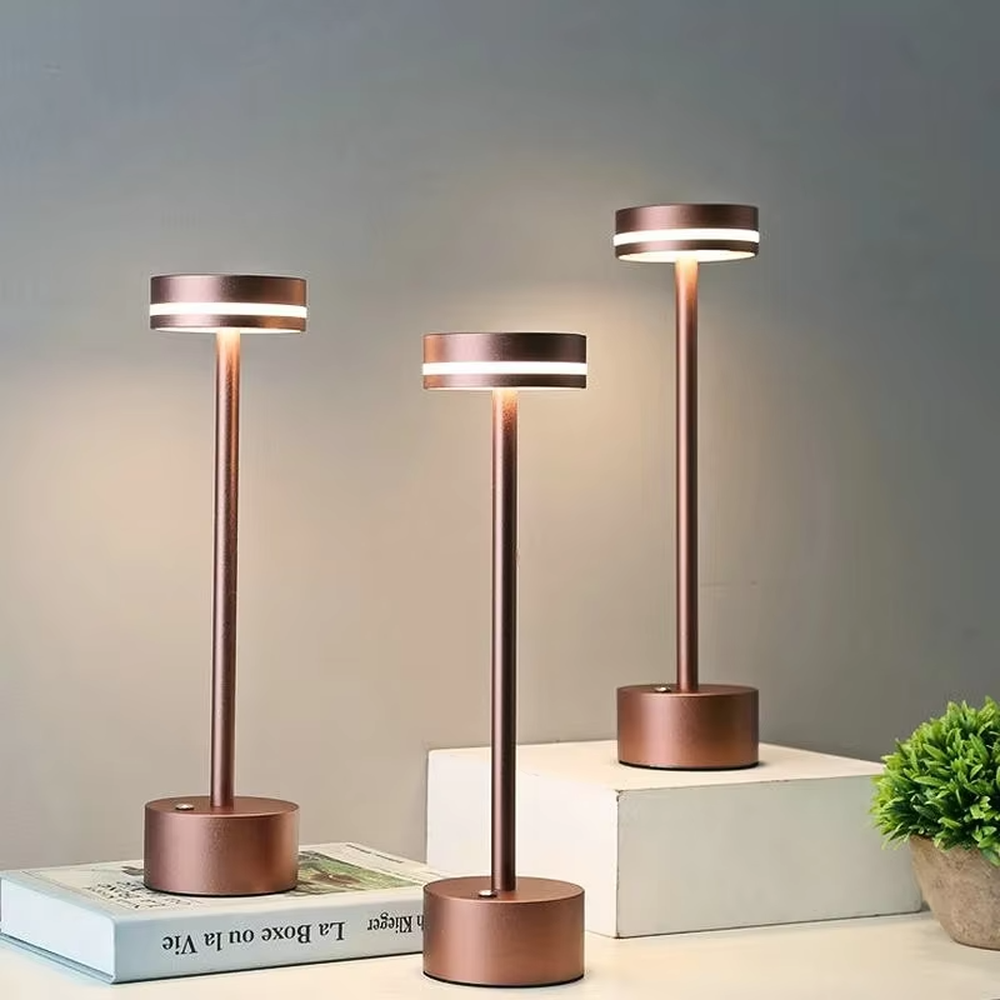 Modern minimalist bronze metal rechargeable table lamp, featuring a cylindrical lamp body and a top ring-shaped lighting design, emitting soft and even light. It supports wireless battery life and touch dimming, suitable for ambient lighting and supplementary lighting in scenarios such as dining tables, bars, and bedroom nightstands.
