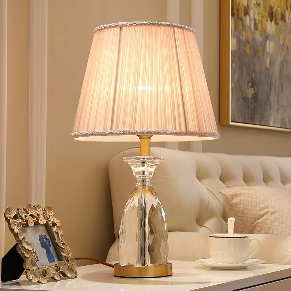 Light luxury crystal table lamp, with a diamond-cut crystal base, pink pleated fabric lampshade and gold metal details, providing soft and warm light, designed to enhance the elegant atmosphere of spaces, suitable for bedroom nightstands, living room side tables, princess rooms, etc.
