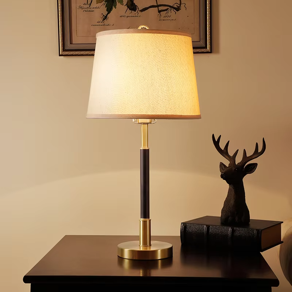This table lamp features a black and gold contrasting metal lamp pole paired with an off-white fabric lampshade, with a glossy gold metal base. It presents a style that combines modern light luxury and minimalist retro, with soft eye-protective light, serving both lighting and decorative purposes, suitable for placement in bedrooms, studies and other spaces.