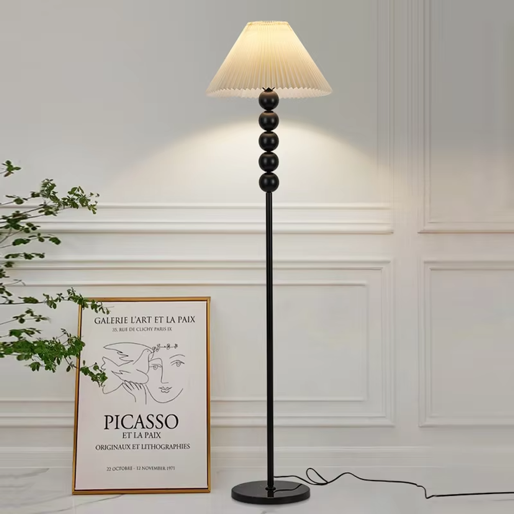 This is a modern minimalist black spherical decorative floor lamp, with a black metal pole featuring spherical decorative elements and a beige pleated fabric lampshade. It has a minimalist and textured design, with soft and warm lighting. It is used for space lighting and decoration, creating a warm and comfortable atmosphere. Suitable for modern minimalist living rooms, bedroom corners, Nordic-style homes and other places.