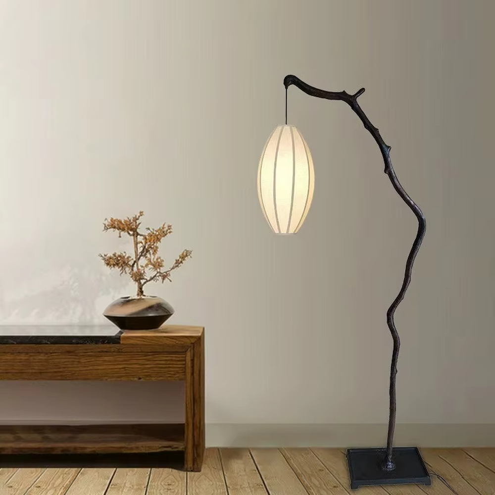 This is a new Chinese Zen-style floor lamp with a dark branch-shaped lamp pole and a beige fabric lantern lampshade. It features a natural and rustic design with a strong Zen sense. It is used for space lighting and decoration, creating a natural Zen ambiance. It is suitable for new Chinese-style home living rooms, Zen teahouses, art homestays and other places.