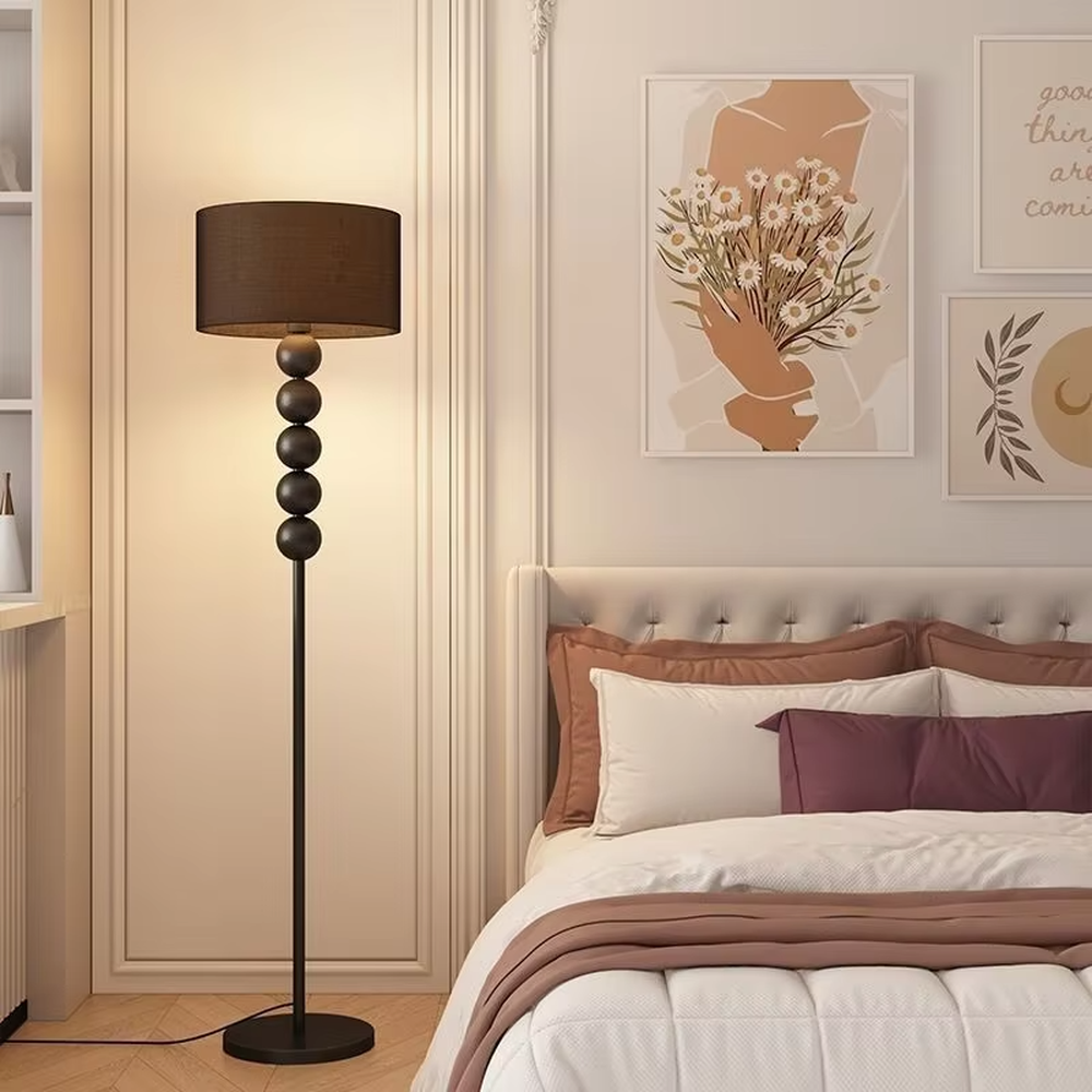 This is a modern warm-style black spherical decorative floor lamp, with a black metal pole featuring spherical decorative elements and a brown fabric lampshade. It has a minimalist and textured design, with soft lighting. It is used for space lighting and decoration, creating a warm and comfortable atmosphere. Suitable for modern minimalist bedrooms, living room corners, Nordic-style homes and other places.