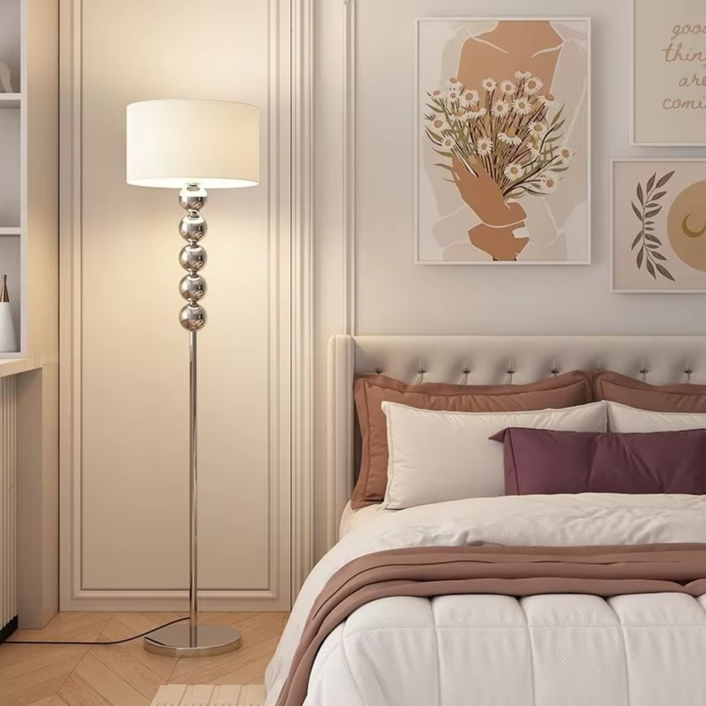 This is a modern warm-style black spherical decorative floor lamp, with a black metal pole featuring spherical decorative elements and a brown fabric lampshade. It has a minimalist and textured design, with soft lighting. It is used for space lighting and decoration, creating a warm and comfortable atmosphere. Suitable for modern minimalist bedrooms, living room corners, Nordic-style homes and other places.