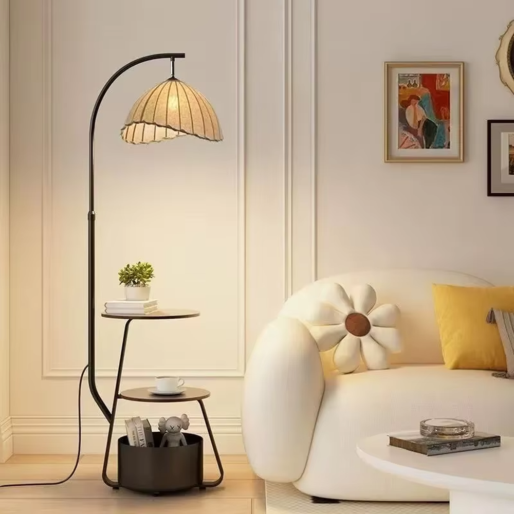 This is a modern multi-functional arc floor lamp with a black metal arc pole, a shell-shaped fabric lampshade, and integrated multi-layer storage shelves, featuring a minimalist and practical design. It is used for space lighting, storage, and decoration, creating a warm and practical atmosphere. It is suitable for modern home living rooms, small-sized residences, leisure reading areas and other places.