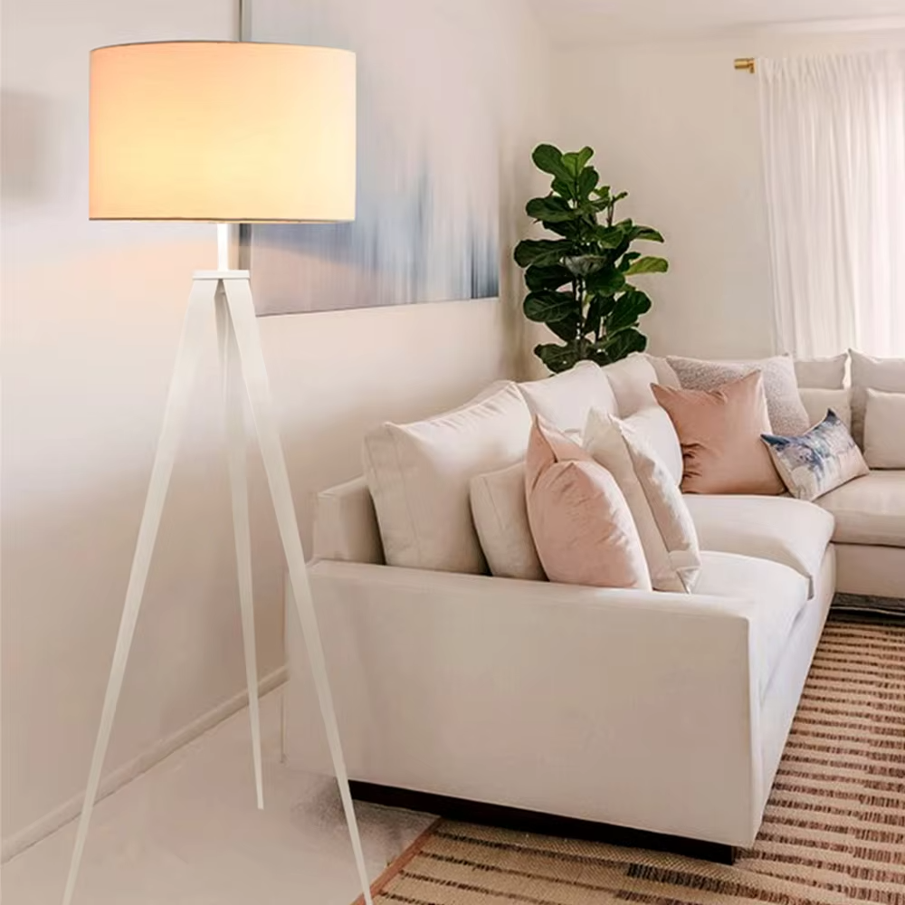 This is a modern minimalist white tripod fabric floor lamp, with a white metal tripod structure and a beige fabric round lampshade. It features a minimalist and grand design, with soft lighting. It is used for space ambient lighting and decoration, creating a modern minimalist atmosphere. Suitable for modern minimalist living rooms, Nordic-style homes, light luxury apartments and other places.
