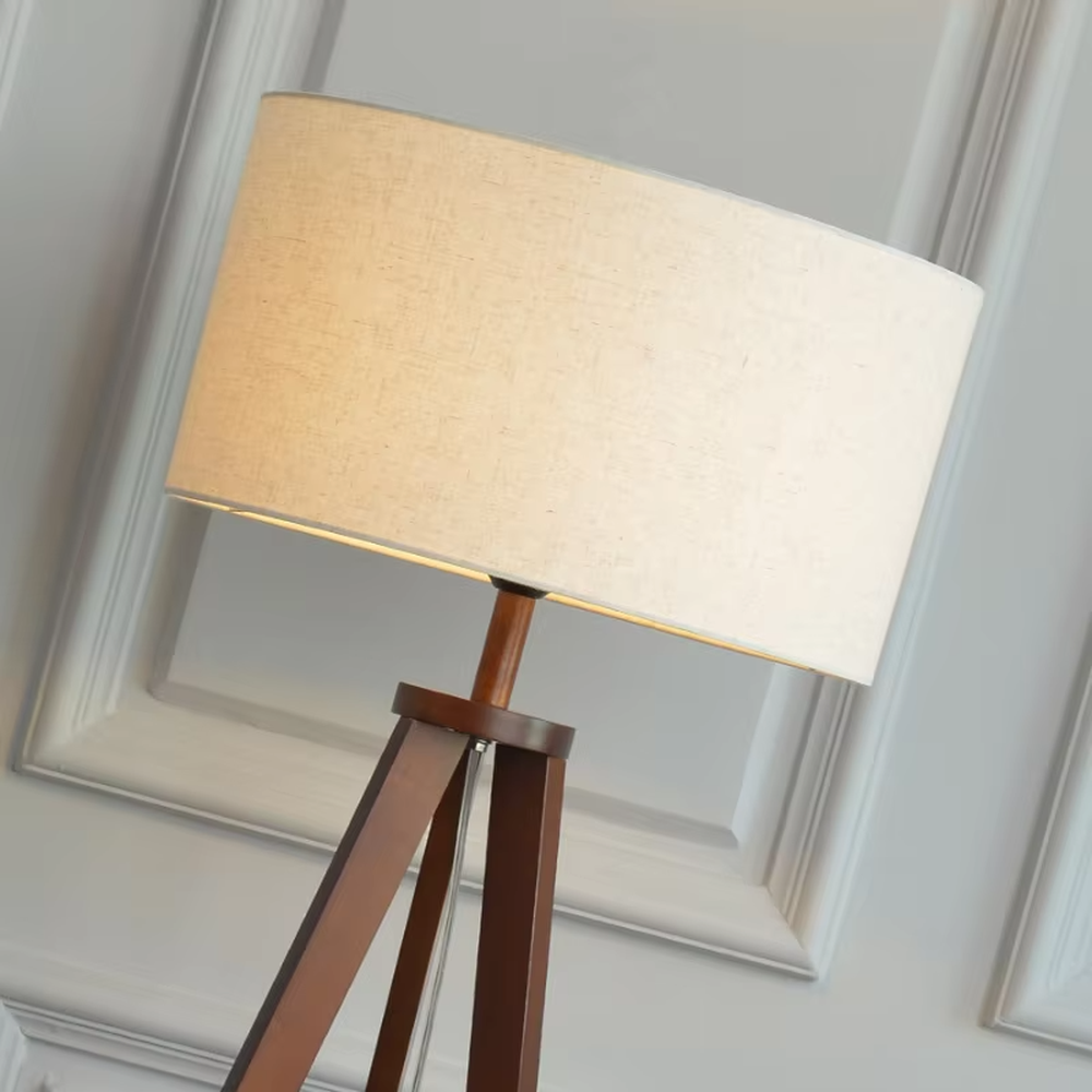 This is a Nordic-style wooden tripod floor lamp, with a light wood tripod stand (with a circular storage table) and a beige fabric cylindrical lampshade, featuring a minimalist and natural design with a warm ambiance. It is used for space lighting and storage decoration, creating a warm and natural atmosphere. It is suitable for Nordic-style home living rooms, minimalist residences, leisure reading areas and other places.