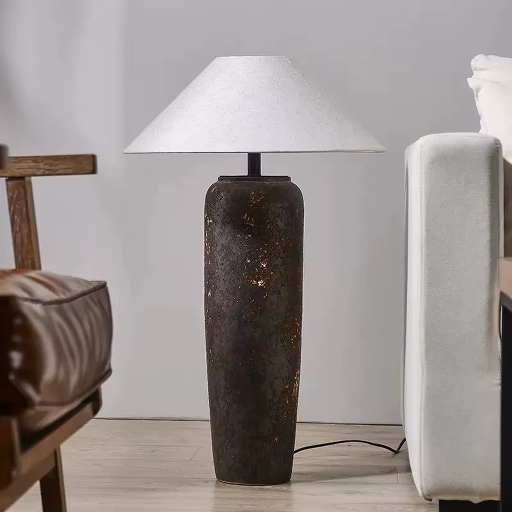 This is a retro industrial-style floor lamp with a dark brown aged texture lamp post and a white fabric slanted lampshade. It features a retro and rustic design with industrial texture. It is used for space lighting and decoration, creating a retro industrial atmosphere. It is suitable for retro industrial-style home living rooms, loft-style apartments, art studios and other places.