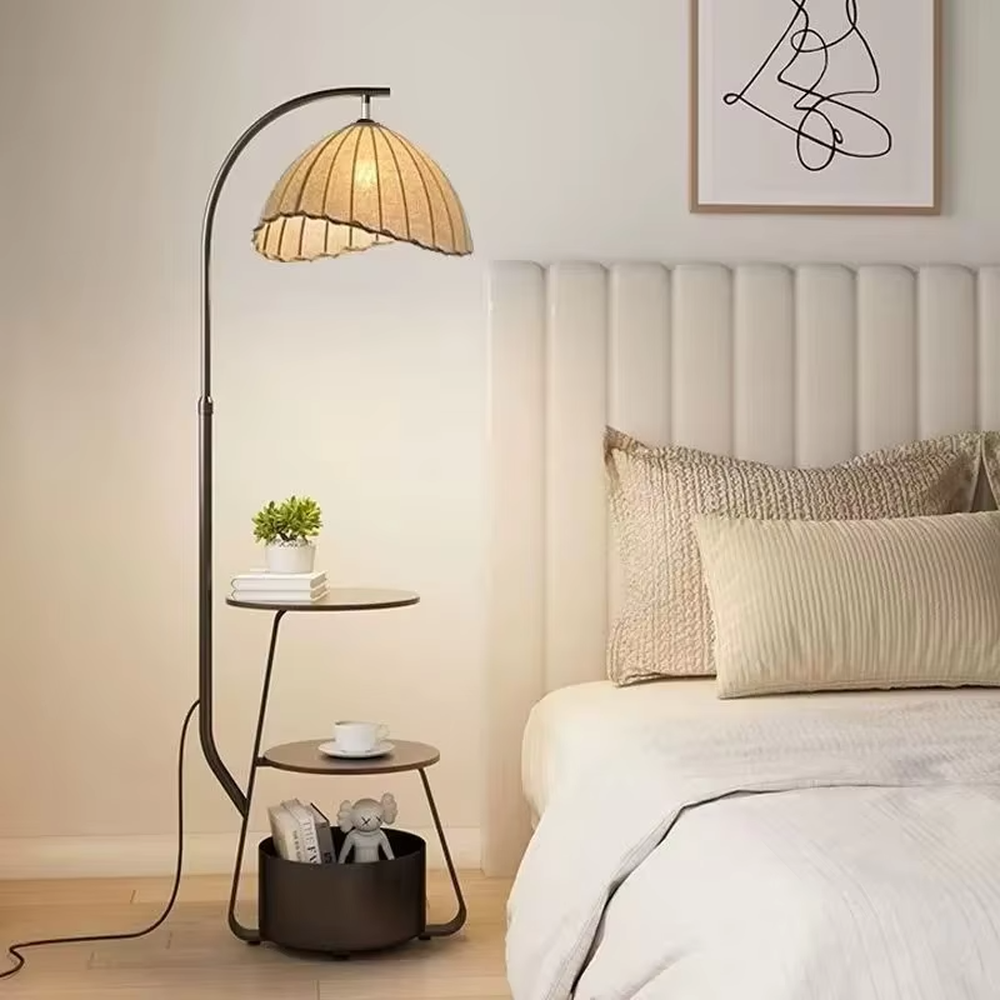 This is a modern multi-functional arc floor lamp with a black metal arc pole, a shell-shaped fabric lampshade, and integrated multi-layer storage shelves, featuring a minimalist and practical design. It is used for space lighting, storage, and decoration, creating a warm and practical atmosphere. It is suitable for modern home living rooms, small-sized residences, leisure reading areas and other places.