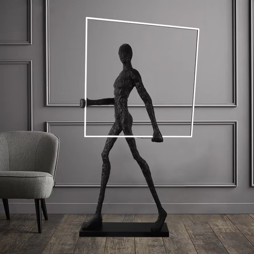 This is an artistic installation-style human sculpture ring floor lamp, featuring a black human sculpture shape paired with a circular LED light. It has a strong sense of art and avant-garde, with soft lighting and visual impact. It is used for space lighting and artistic decoration, creating a modern artistic and avant-garde atmosphere. Suitable for art exhibition halls, high-end villa living rooms, designer studios and other places.