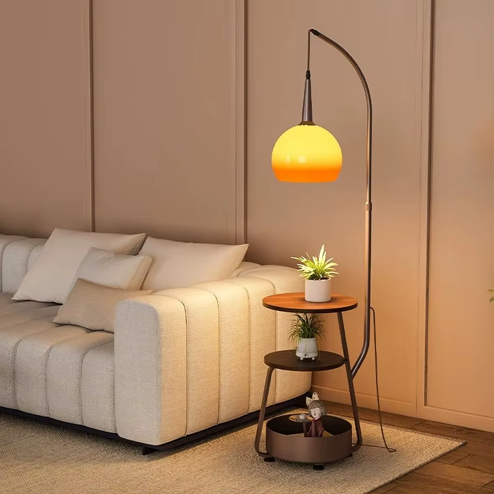 This is a modern multi-functional floor lamp with a curved metal pole, a gradient orange-yellow spherical lampshade, and integrated multi-layer storage shelves, featuring a minimalist and practical design. It is used for space lighting, storage, and decoration, creating a warm and practical atmosphere. It is suitable for modern home living rooms, small-sized residences, creative studios and other places.