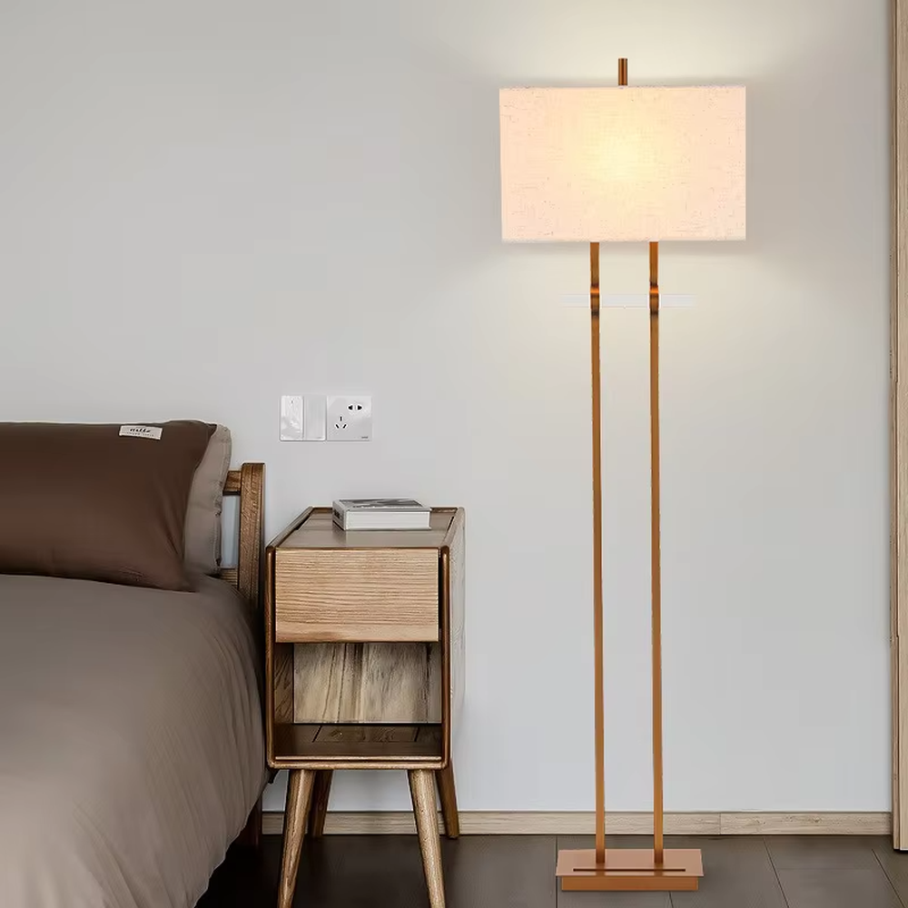This is a modern minimalist metal double-pole floor lamp, with golden metal double poles and a beige fabric square lampshade, featuring a minimalist and grand design, modern style. It is used for space lighting and decoration, creating a minimalist and warm atmosphere. It is suitable for modern minimalist home bedrooms, living room corners, studies and other places.