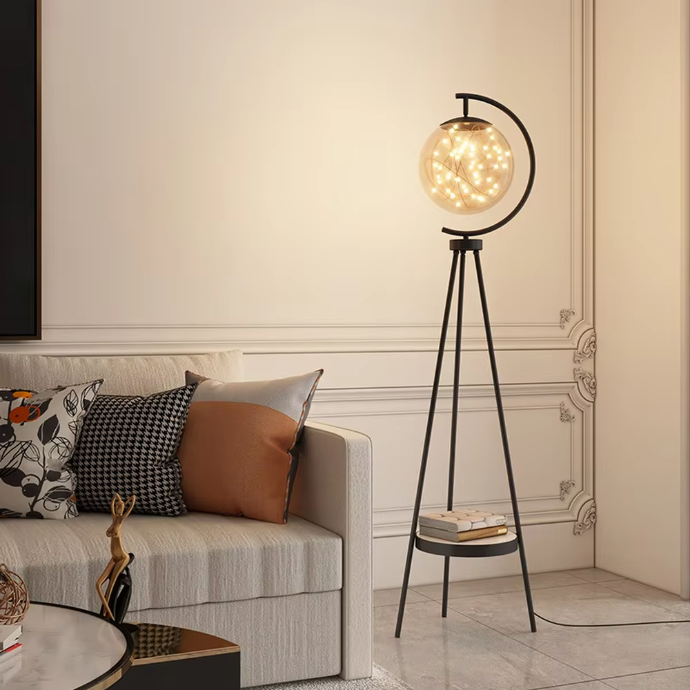 This is a light luxury modern-style golden tripod glass ball floor lamp, with a golden tripod structure, a transparent glass ball (with built-in light string) and a small tray, featuring an exquisite light luxury design, warm lighting. It is used for space lighting and decoration, creating a light luxury and warm atmosphere. Suitable for modern light luxury living rooms, bedroom corners, Nordic-style homes and other places.