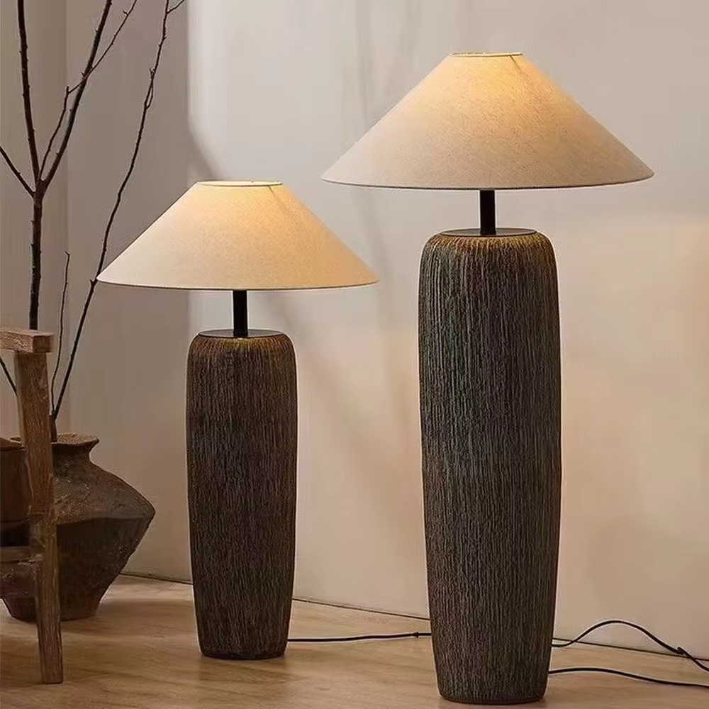 This is a natural wabi-sabi style gray textured column floor lamp, with a gray textured column base, a beige fabric conical lampshade, and a black metal pole connection. It features a minimalist and natural design with a rustic texture. It is used for space lighting and decoration, creating a warm and rustic atmosphere. Suitable for wabi-sabi style living rooms, Japanese-style bedrooms, natural-style homestays and other places.
