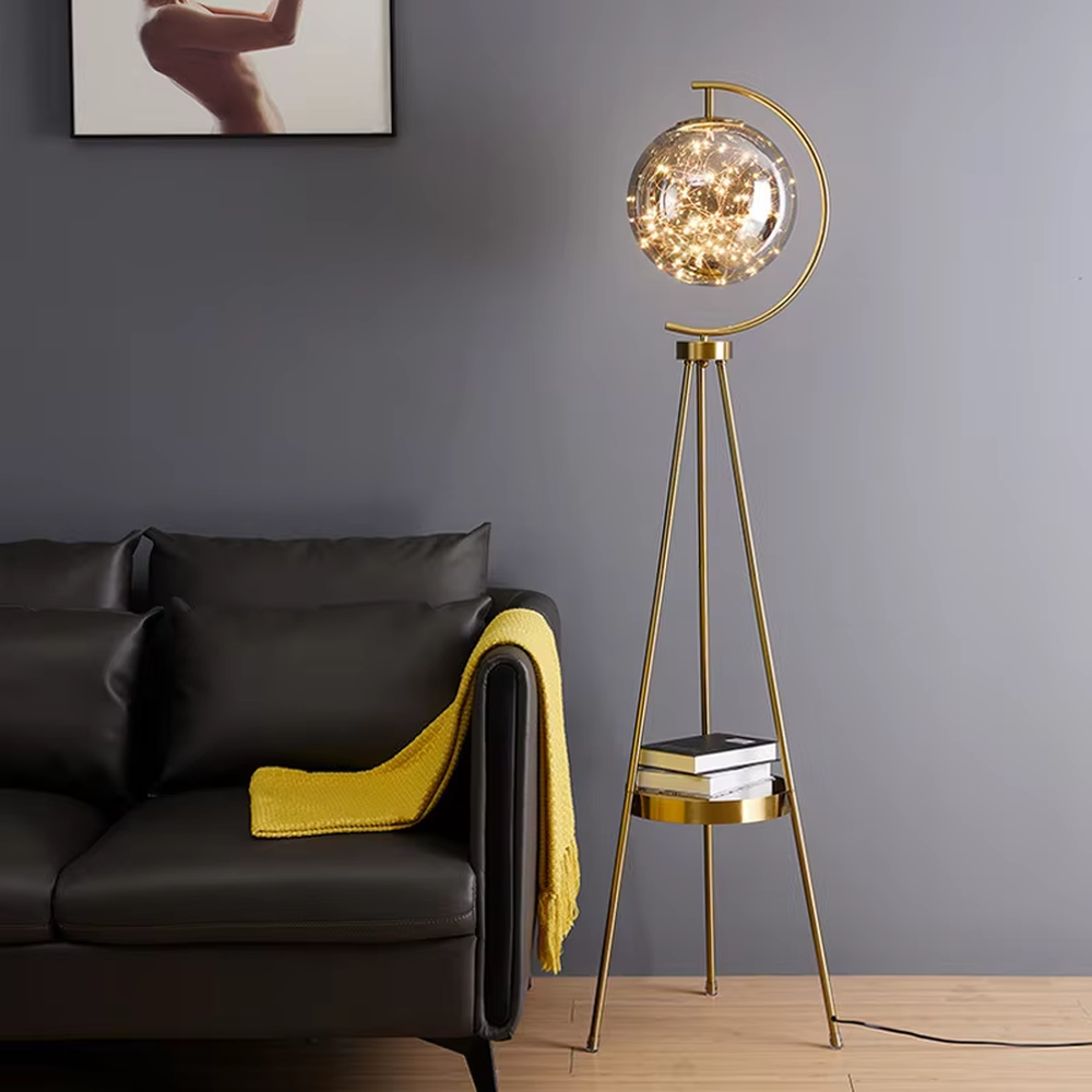 This is a light luxury modern-style golden tripod glass ball floor lamp, with a golden tripod structure, a transparent glass ball (with built-in light string) and a small tray, featuring an exquisite light luxury design, warm lighting. It is used for space lighting and decoration, creating a light luxury and warm atmosphere. Suitable for modern light luxury living rooms, bedroom corners, Nordic-style homes and other places.