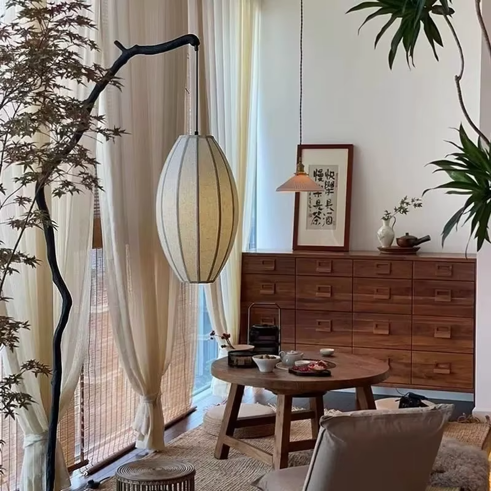 This is a new Chinese Zen-style floor lamp with a dark branch-shaped lamp pole and a beige fabric lantern lampshade. It features a natural and rustic design with a strong Zen sense. It is used for space lighting and decoration, creating a natural Zen ambiance. It is suitable for new Chinese-style home living rooms, Zen teahouses, art homestays and other places.