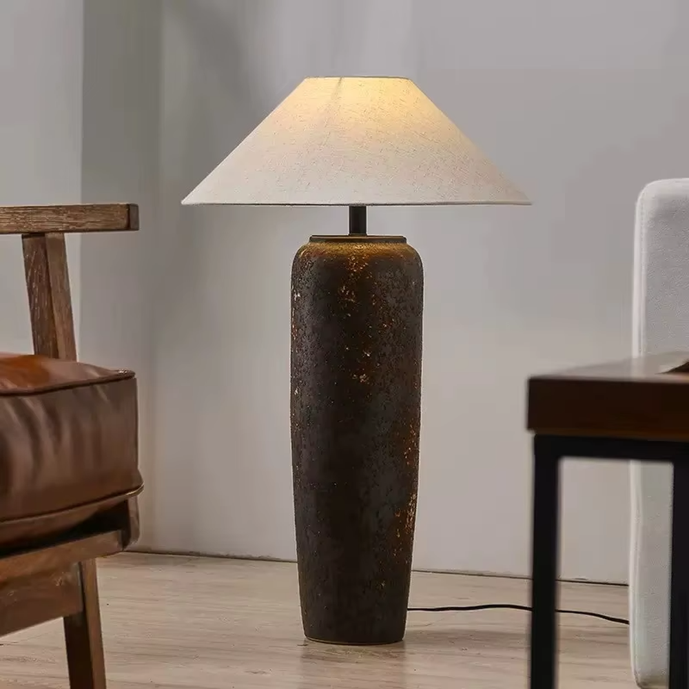 This is a retro industrial-style floor lamp with a dark brown aged texture lamp post and a white fabric slanted lampshade. It features a retro and rustic design with industrial texture. It is used for space lighting and decoration, creating a retro industrial atmosphere. It is suitable for retro industrial-style home living rooms, loft-style apartments, art studios and other places.