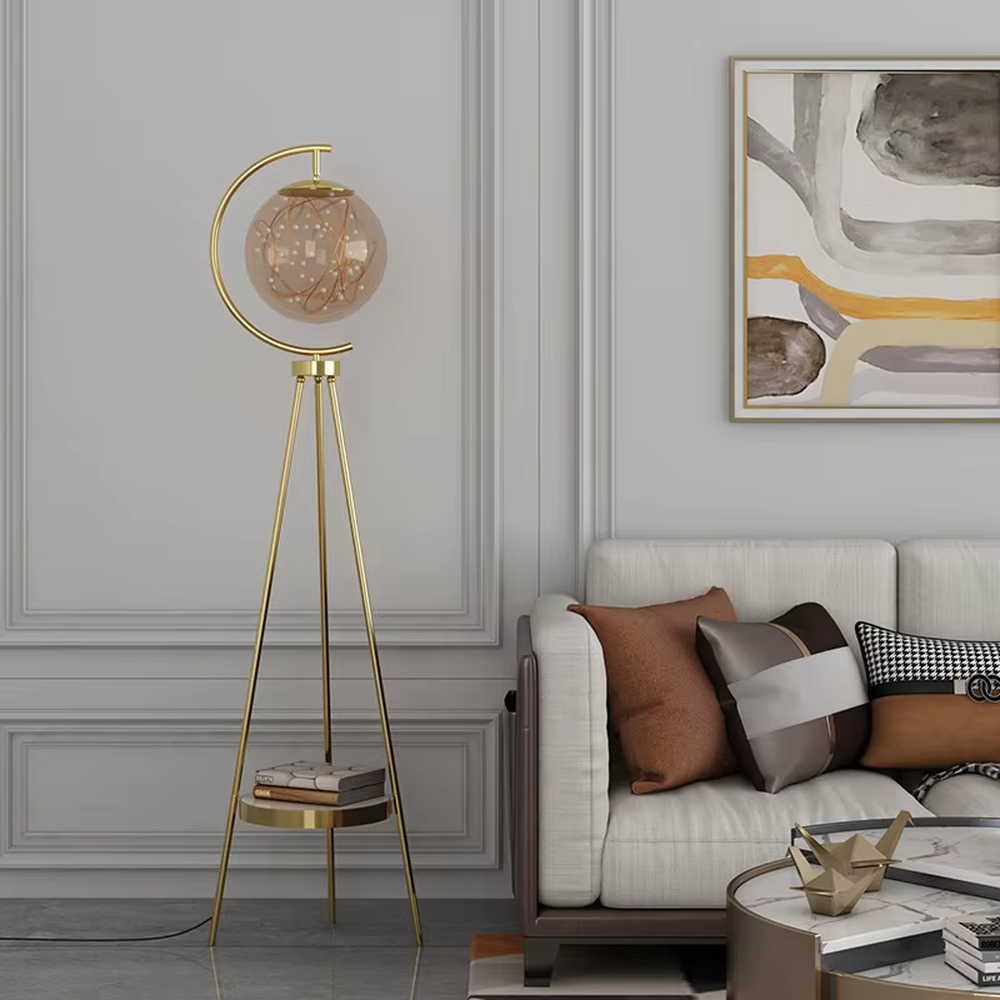 This is a light luxury modern-style golden tripod glass ball floor lamp, with a golden tripod structure, a transparent glass ball (with built-in light string) and a small tray, featuring an exquisite light luxury design, warm lighting. It is used for space lighting and decoration, creating a light luxury and warm atmosphere. Suitable for modern light luxury living rooms, bedroom corners, Nordic-style homes and other places.
