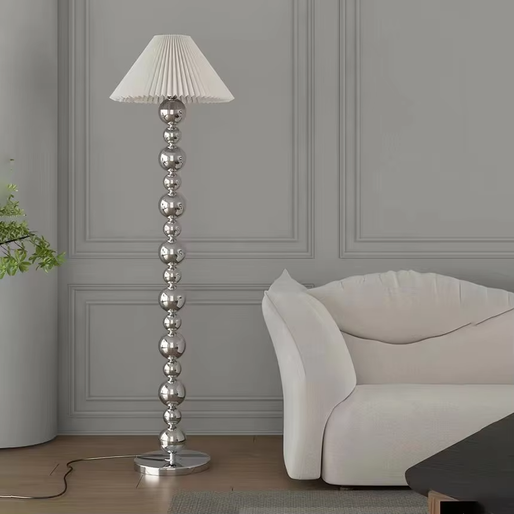 This is a light luxury exquisite silver metal ball column floor lamp, with silver metal balls layered to form a column, paired with a beige fabric round lampshade. It features a light luxury and exquisite design, with soft lighting. It is used for space ambient lighting and decoration, creating a light luxury elegant atmosphere. Suitable for light luxury-style living rooms, modern minimalist bedrooms, high-end hotel guest rooms and other places.