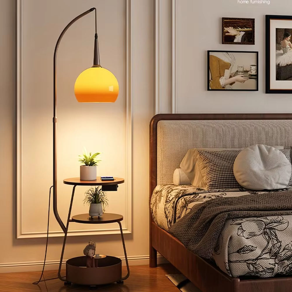 This is a modern multi-functional floor lamp with a curved metal pole, a gradient orange-yellow spherical lampshade, and integrated multi-layer storage shelves, featuring a minimalist and practical design. It is used for space lighting, storage, and decoration, creating a warm and practical atmosphere. It is suitable for modern home living rooms, small-sized residences, creative studios and other places.