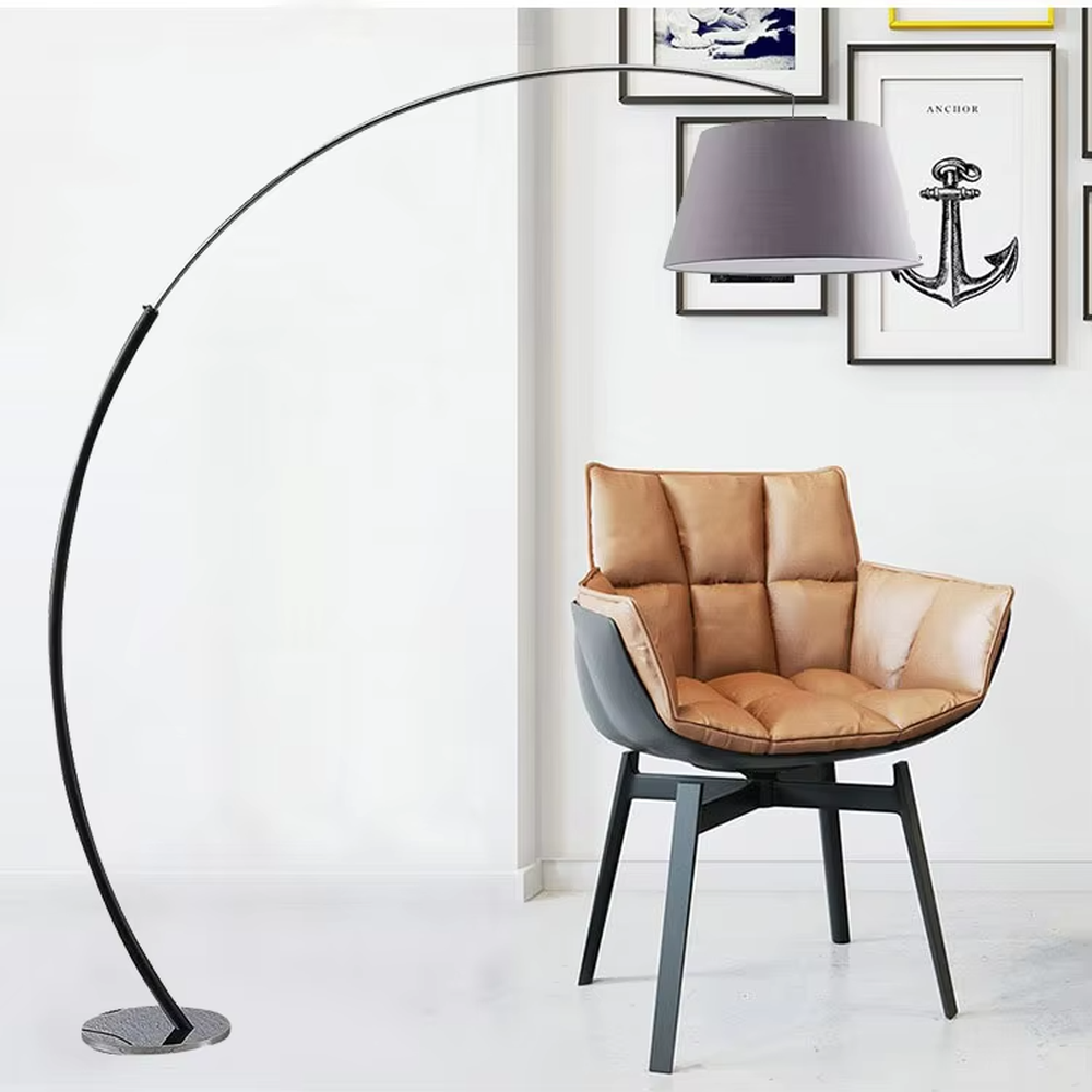 This is a modern minimalist curved floor lamp, with a black curved lamp pole paired with a light purple fabric lampshade and a silver textured disc base. The lighting is soft and warm, creating a minimalist comfortable atmosphere.